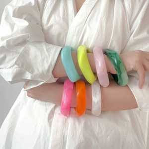 Close-up of a model wearing seven colorful chunky resin bangles with a glossy finish