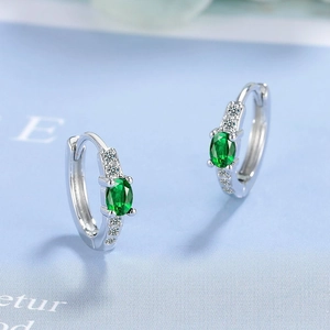 Detail of silver hoop earrings featuring oval green gemstones and white diamond accents