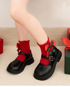 Close-up of red Christmas socks with bows and green pom-poms worn with Mary Jane shoes