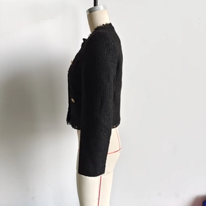 Detailaufnahme der schwarzen Tweed-Jacke mit metallischer Textur und Goldknöpfen