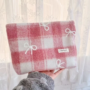 Detail of pink plaid tweed makeup bag with white embroidered bow and brand label