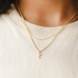 Layered gold necklace featuring a gothic letter E pendant on curb and cable chains
