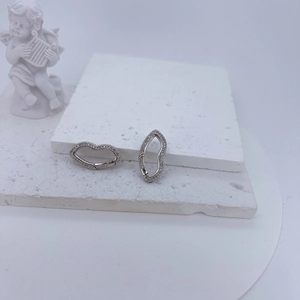 Detailed view of silver lip-shaped earrings with cubic zirconia on white plaster