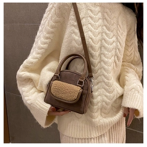 Detail of dark brown faux suede bag with lamb wool pocket on a white cable knit sweater