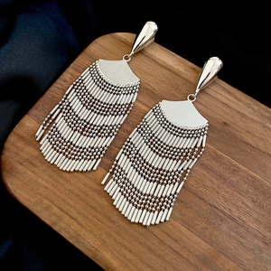 Detail of silver fan-shaped tassel earrings on a wooden tray with a dark velvet background