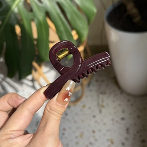 Detail of burgundy glossy hair claw clip with golden metal spring held by hand