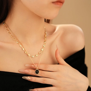 Close-up of double-layered gold-plated heart necklace with black gemstone pendant on model