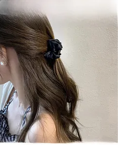 Detail of elegant black satin flower hair claw clip on brunette wavy hair for styling