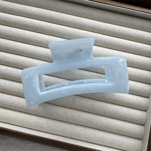 Macro detail of a light blue rectangular hair claw clip with ink marble texture on beige tray