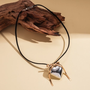 Detail shot of a silver heart pendant with a gold bow on a black velvet cord