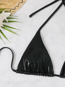Flat lay of black metallic triangle bikini top on white marble background with summer props