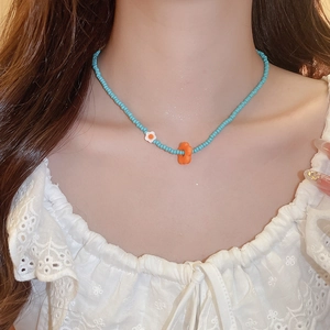 Detail view of light blue beaded necklace with orange and white floral pendants on model
