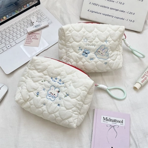 Detail of white heart quilted makeup bag with cute rabbit embroidery and red zipper