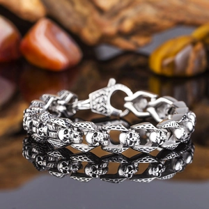Macro shot of silver skull link bracelet with vintage finish on a reflective black surface