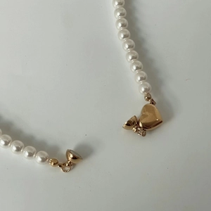 Detailed macro view of a gold heart magnetic clasp on a white pearl beaded necklace