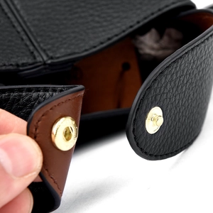Close-up of black leather handbag with gold snap button and brown interior lining