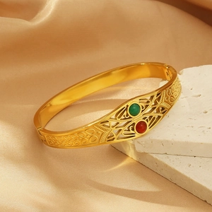 Irregular gold hollow geometric bangle with green and red cat-eye stones on white stone base
