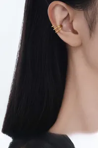 Macro close-up of a minimalist golden double hoop ear cuff on a female model's ear