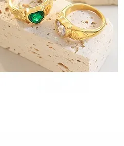 Detail of gold heart rings with green and clear stones on textured stone base