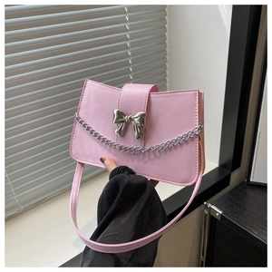Close-up of pink leather handbag featuring a silver bow metal piece and thin decorative chain