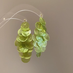 Green shell circular tassel drop earrings with gold metal studs on reflective stand