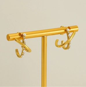 Macro shot of gold-plated X-cross earrings with delicate white pearls and crystals