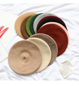 Flat lay of colorful wool beret hats stacked in beige green and red tones