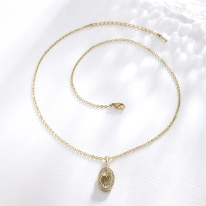Elegant gold-tone oval pendant necklace set with clear crystals on textured background