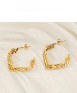 Gros plan de boucles d'oreilles torsadées dorées sur un fond de tissu en soie blanche