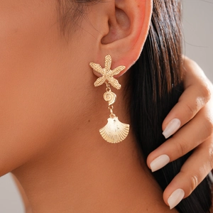 Close-up of golden starfish and seashell drop earrings on model for beach style