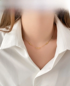 Close-up of a gold beaded necklace on a model wearing a white shirt for a refined look