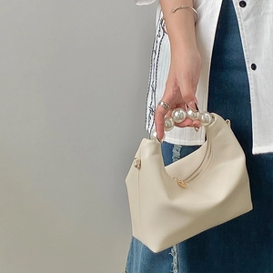 Detail of a creamy white pearl handle handbag with elegant beaded strap and soft material
