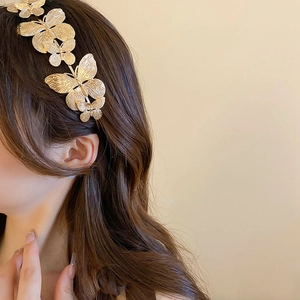 Detail of a golden metal butterfly headband featuring brushed texture on a model
