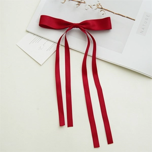 Detail of red satin bow hair clip with long flowing ribbons on a rustic nature background