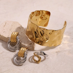 Bracciale rigido dorato con orecchini e anello bicolore su trama in pietra naturale