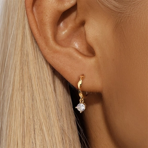 Close-up of golden twisted hoop earrings with a sparkling zircon pendant worn by model