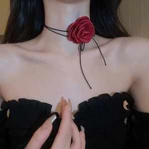 Detail view of a handmade red fabric rose choker with a black cord on a model