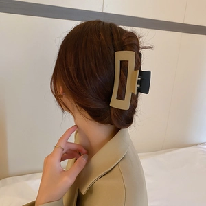 Détail d'une grande pince à cheveux beige en acrylique portée sur des cheveux bruns