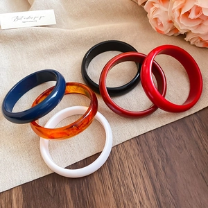 Set of six colorful resin bangles in blue, amber, and red on a soft beige linen texture