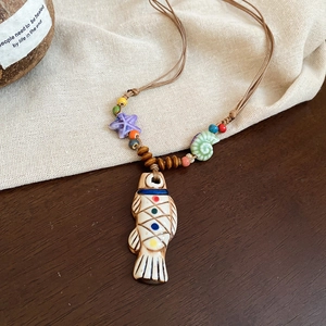 Detail of handcrafted ceramic fish pendant with colorful beads on a wooden surface
