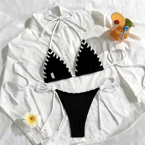 Bikini côtelé noir et blanc avec lacets, vue à plat dans une ambiance de vacances tropicales