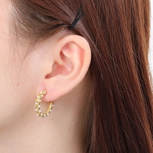 Macro close-up of C-shaped gold pearl stud earrings worn on a female model