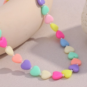 Colorful acrylic heart bead necklace with small white spacers on a beige display stand