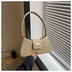 Detail of a beige baguette bag with a gold buckle held by a model in soft natural light