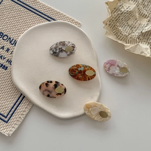 Elegant oval acetate hair clips in leopard and marble patterns on a ceramic tray