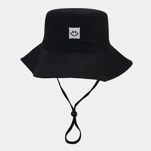 Detailed view of black bucket hat featuring a smiley face patch and adjustable wind rope