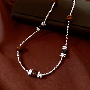 Détail du collier de perles en œil de tigre et perles argentées sur tissu texturé