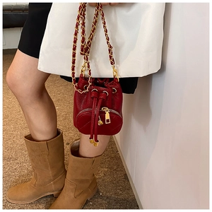 Red quilted drawstring bucket bag with gold chain strap shown on model for scale