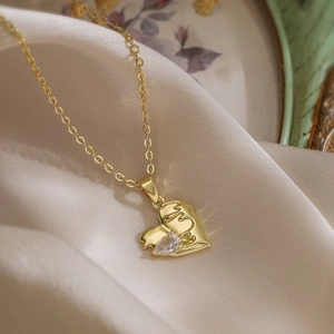 Minimalist gold hugging heart necklace with a sparkling teardrop zircon on beige silk