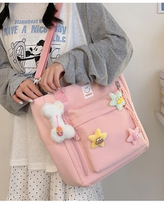 Pink nylon tote bag with plush star charms and front pocket detail on female model